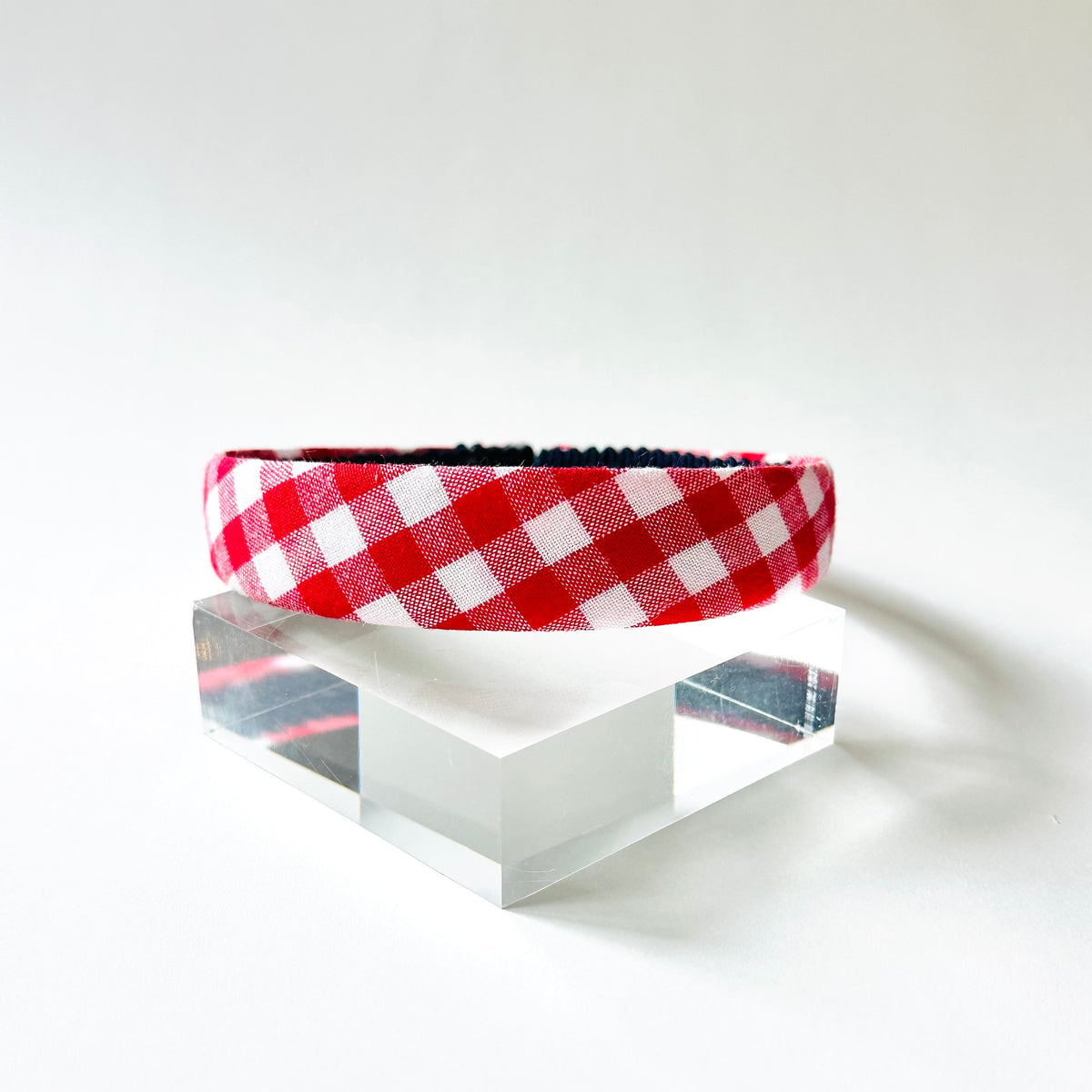 Red and white checkered headband on a clear stand against a white background