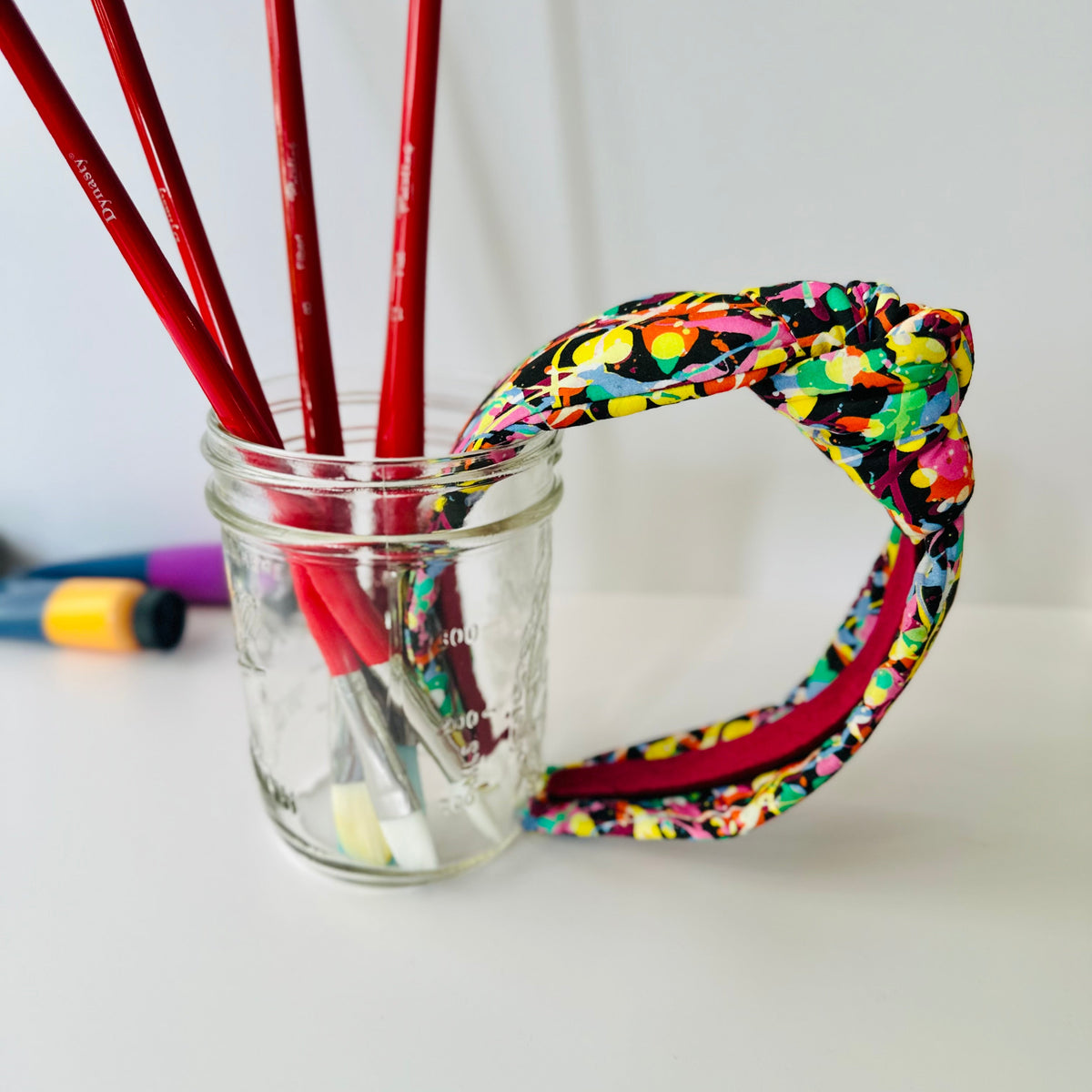 Colorful headband with red pencils in a glass jar on a white surface