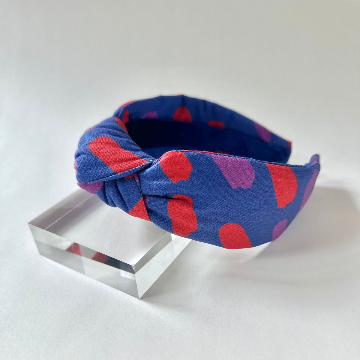 Blue headband with red and purple abstract pattern on a clear stand against a white background