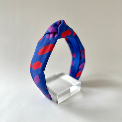 Blue headband with red and purple polka dots on a clear stand against a beige background