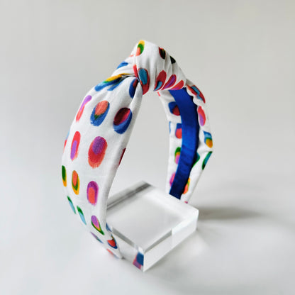 Colorful polka dot headband on a white stand against a light gray background