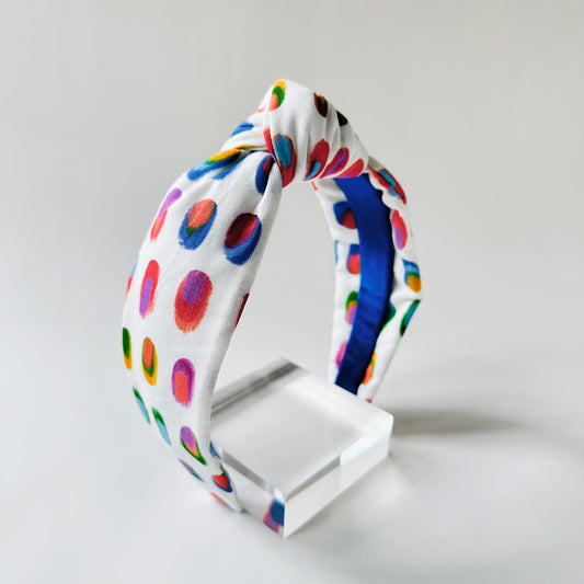 Colorful polka dot headband on a white stand against a light gray background