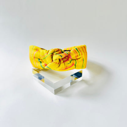 Yellow headband with floral pattern on a clear stand against a white background