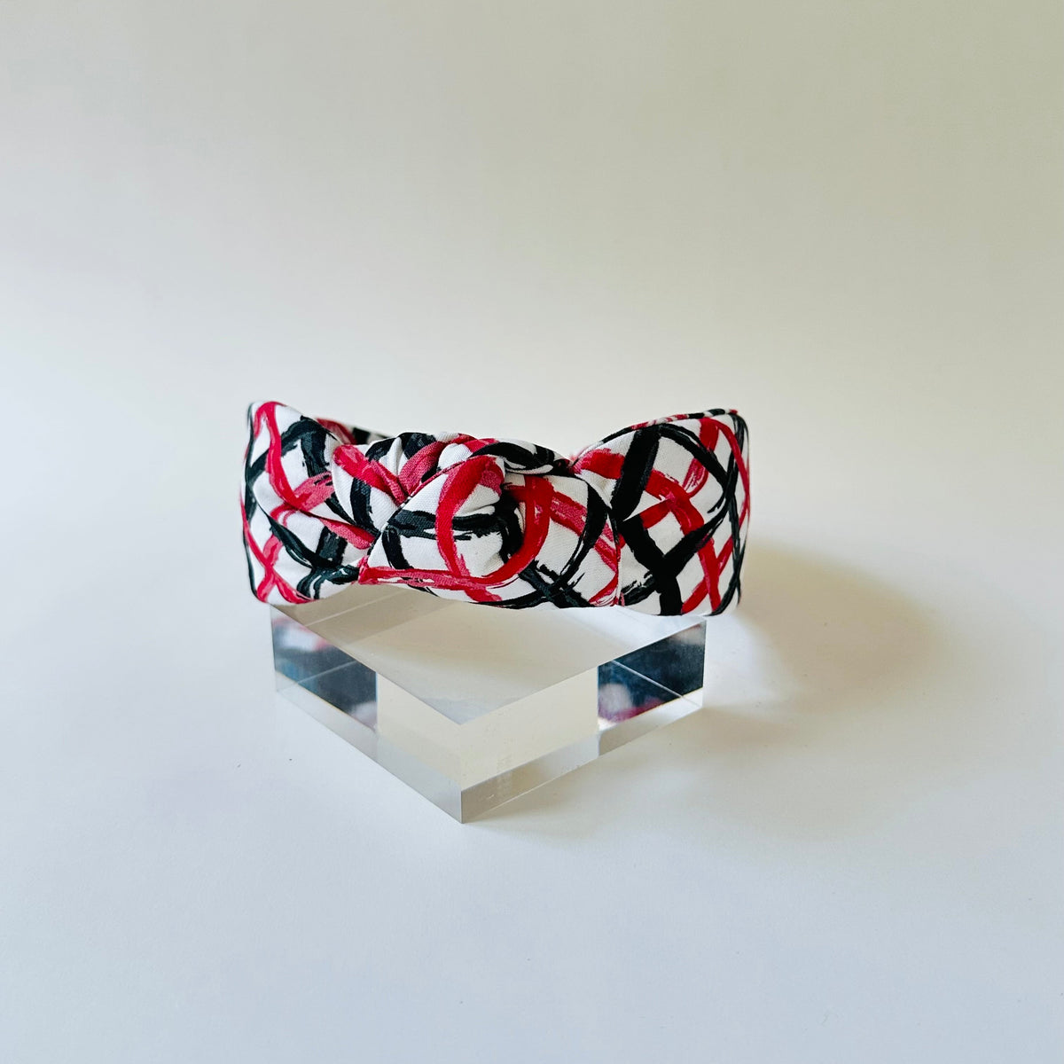 Headband with red and black pattern on a clear stand against a white background