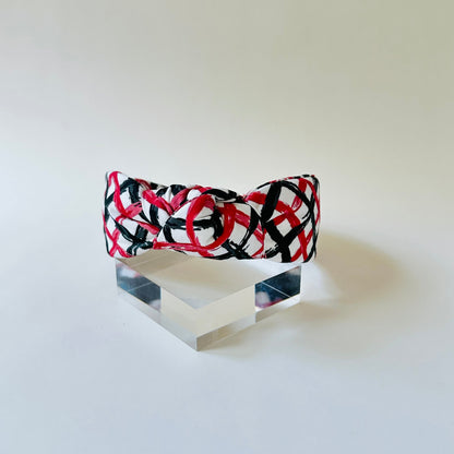 Headband with red and black pattern on a clear stand against a white background