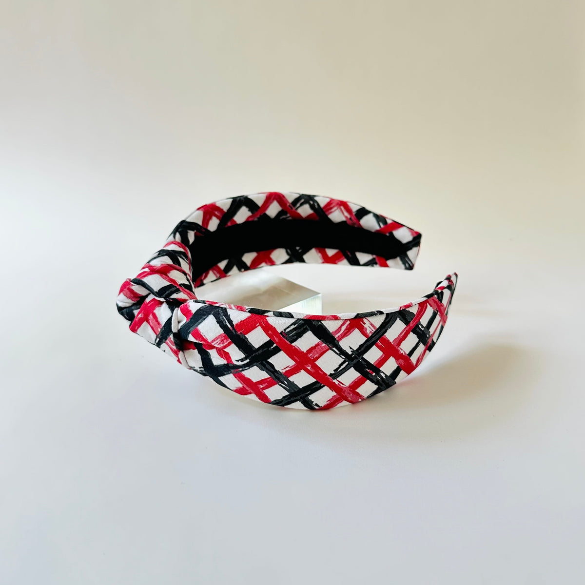 Plaid headband with red, black, and white pattern on a light gray background